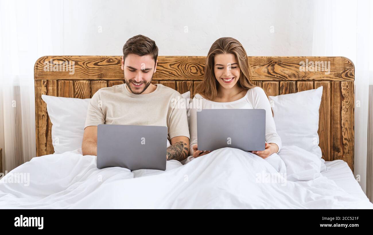 Loisirs ensemble. Jeune mari et femme assis sur le lit et regardant les ordinateurs portables Banque D'Images