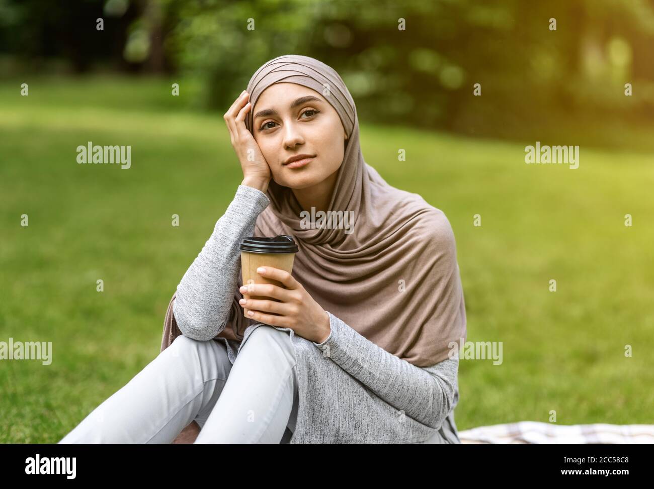 Une jeune fille arabe rêveuse assise seule au parc, buvant du café Banque D'Images