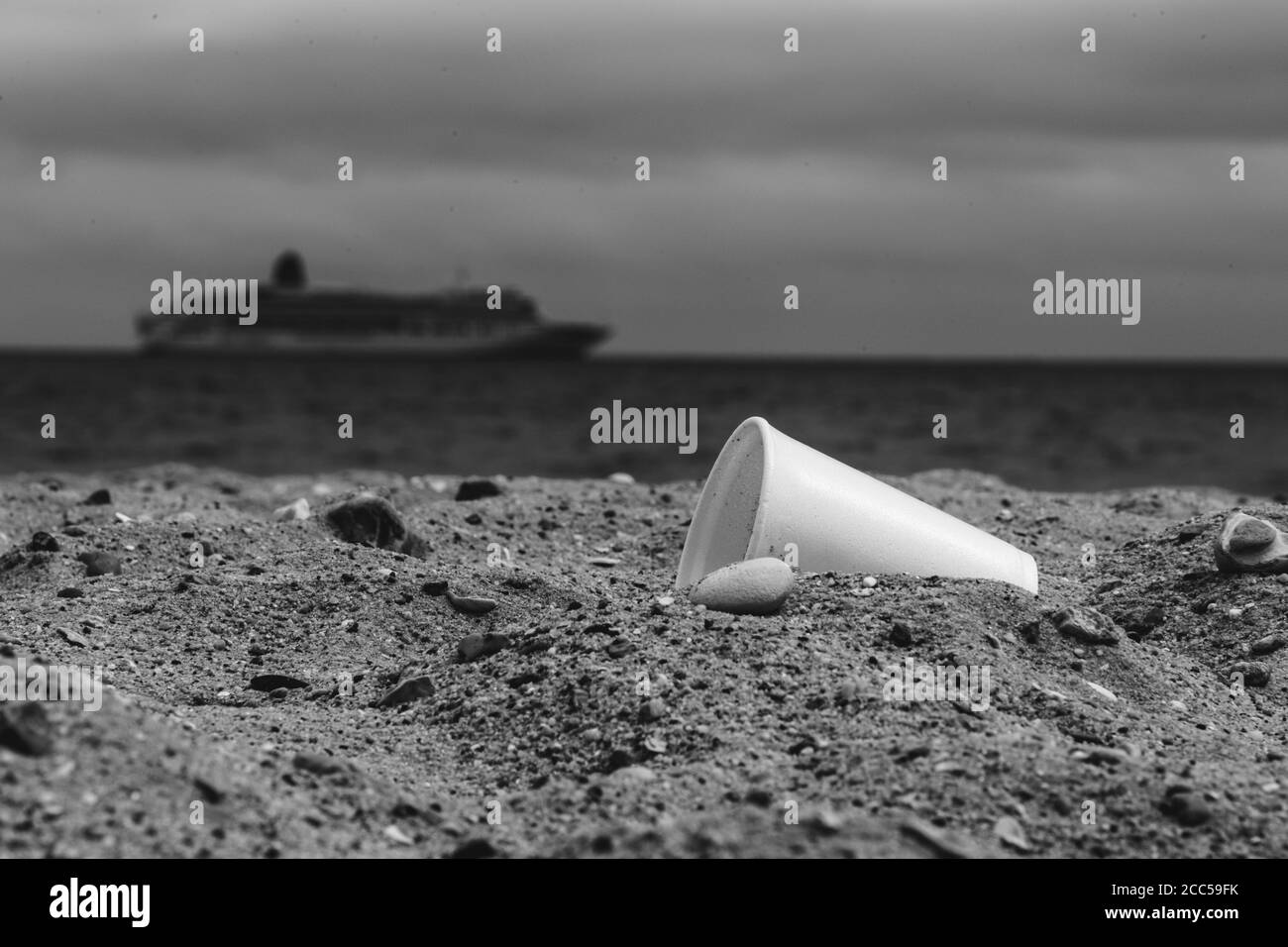 Pollution plastique : coupe Styrofoam laissée par les touristes sur la plage. Bateau de croisière en arrière-plan. Bournemouth, Royaume-Uni. Banque D'Images