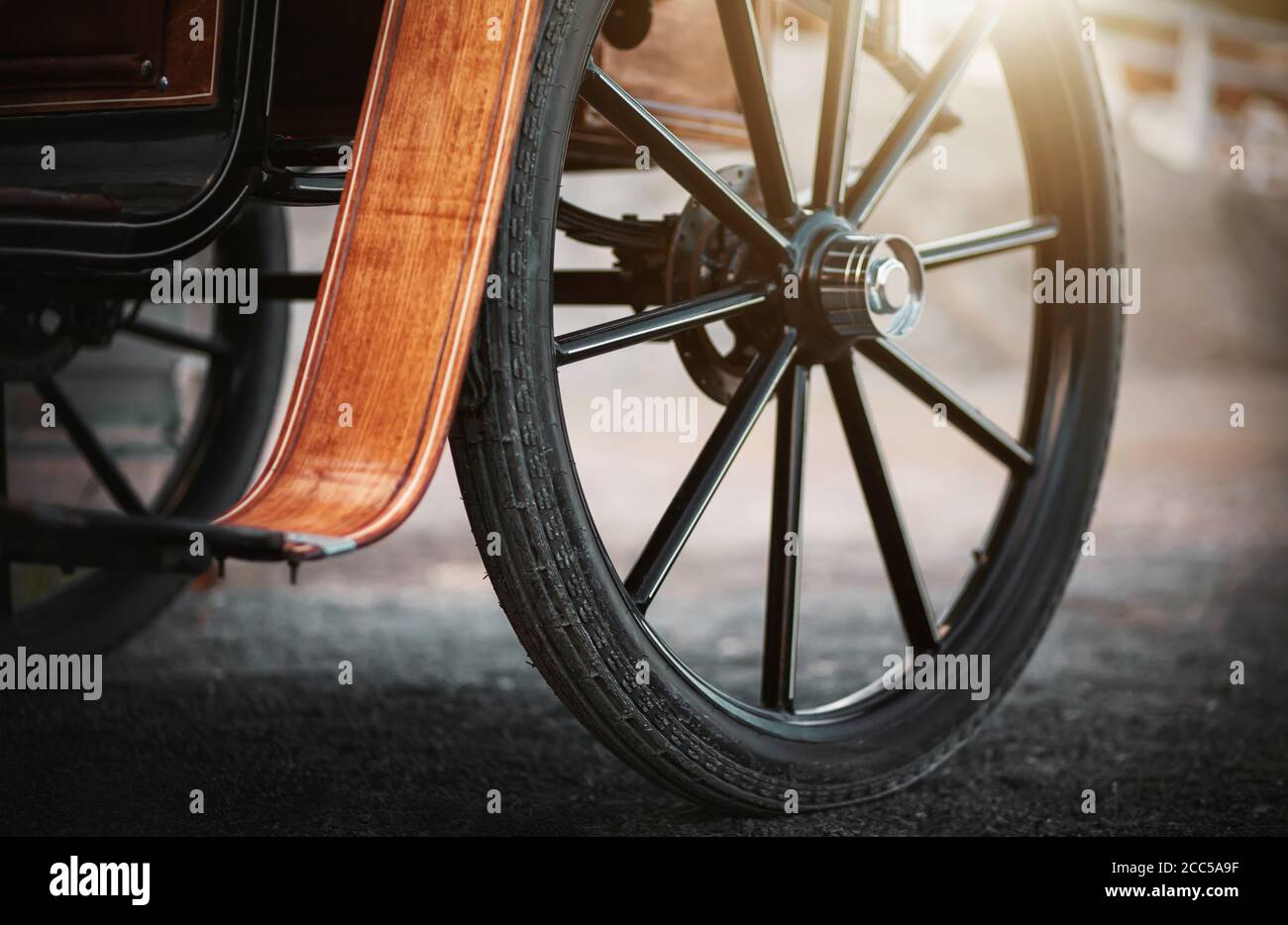 Une grande roue sombre sur une ancienne calèche avec des éléments en bois pour les chevaux, qui est illuminée par les rayons du soleil. Histoire. Banque D'Images