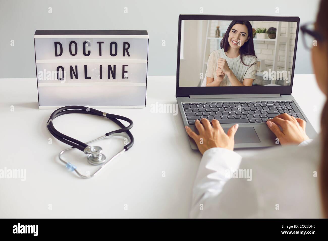 Médecin en ligne. Le patient et le médecin utilisent un ordinateur portable en ligne avec appel vidéo. Le médecin consulte à distance tout en étant assis à la table dans le bureau du Banque D'Images