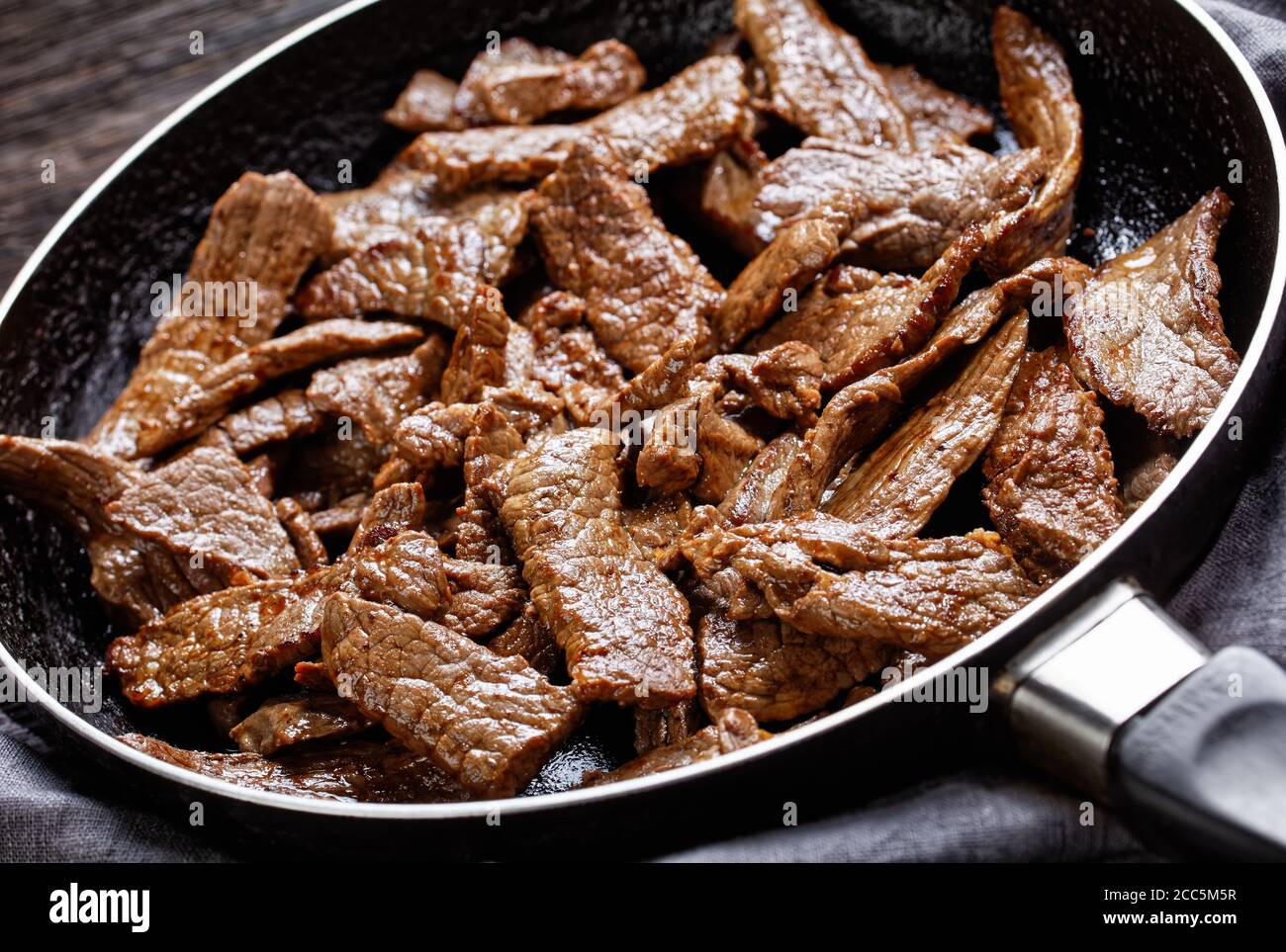 steak de bœuf à la ribeye poêlé tendre et juteux coupé en lanières, steak minute, sur une poêle sur une table en bois sombre, vue horizontale depuis le dessus Banque D'Images