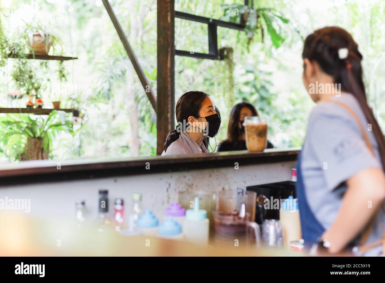 Femme cliente en masque facial donnant la commande à la serveuse à comptoir de café Banque D'Images