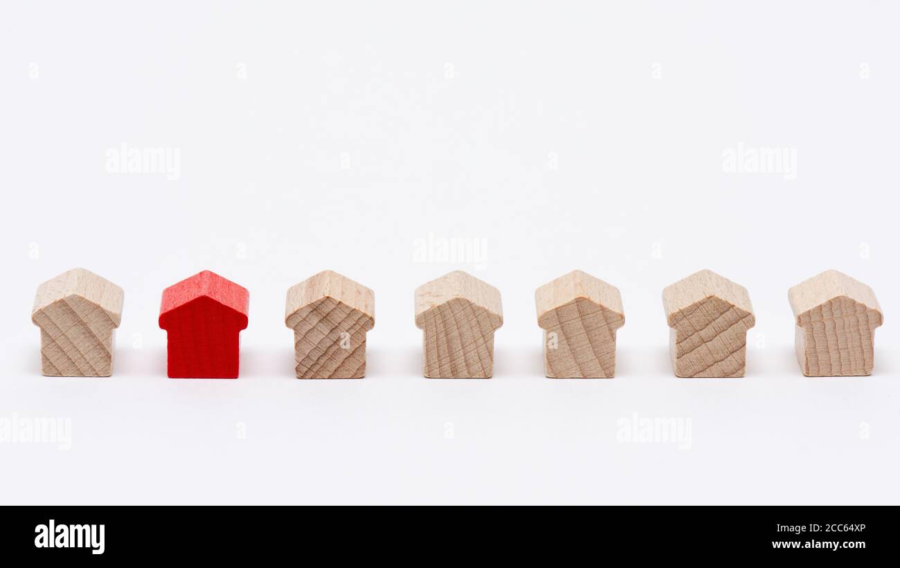 Petites maisons de jouets en bois dans une rangée, l'une d'entre elles peint rouge, blanc fond Banque D'Images