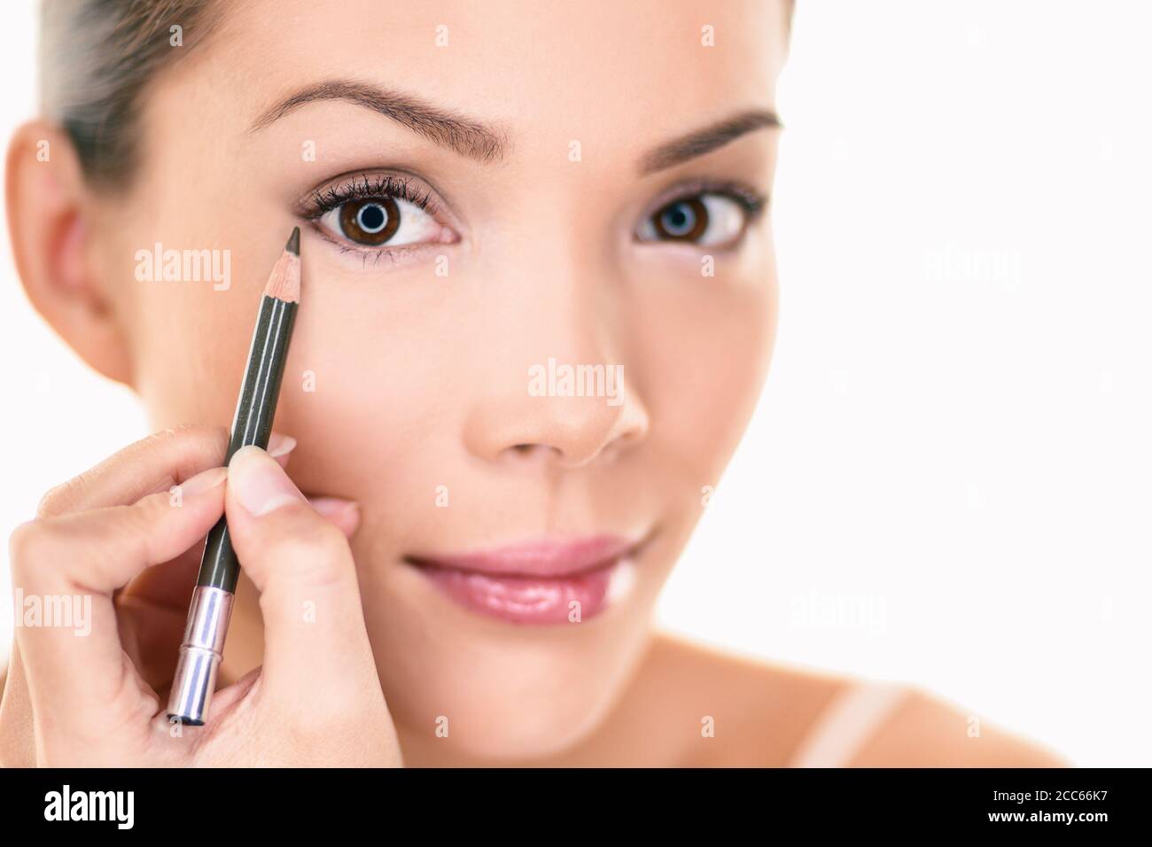 Femme asiatique se préparer application de crayon à paupières brun sur les yeux regardant dans le miroir. Isolé sur fond blanc Banque D'Images
