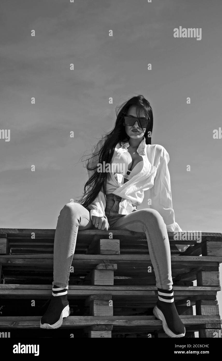 Photo de mode de fille sexy assise sur des palettes et posant sur le ciel bleu Banque D'Images