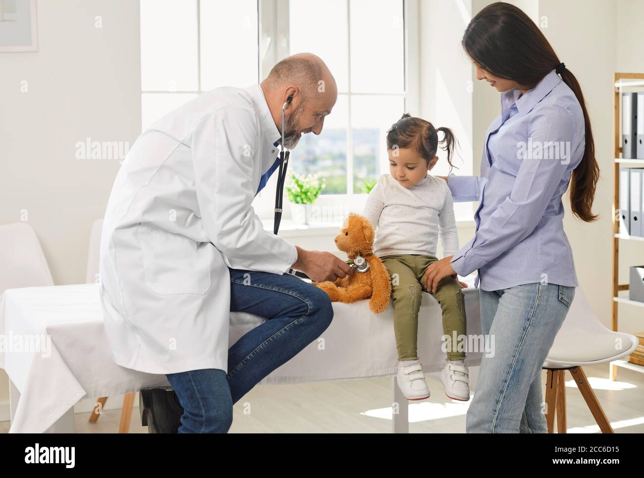 Un médecin expérimenté avec un stéthoscope écoute une petite fille avec des mères de patients à l'hôpital. Banque D'Images