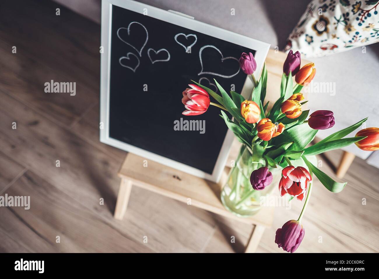 Des tulipes colorées dans un vase avec un tableau de chalk sont au sol dans la salle de séjour Banque D'Images