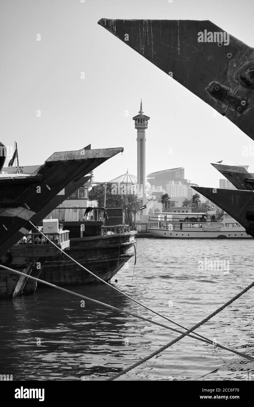 Arcs de navires arabes à Deira et minaret de la mosquée Garand de l'autre côté de la crique de Dubaï, Dubaï, Émirats Arabes Unis. Photographie en noir et blanc Banque D'Images