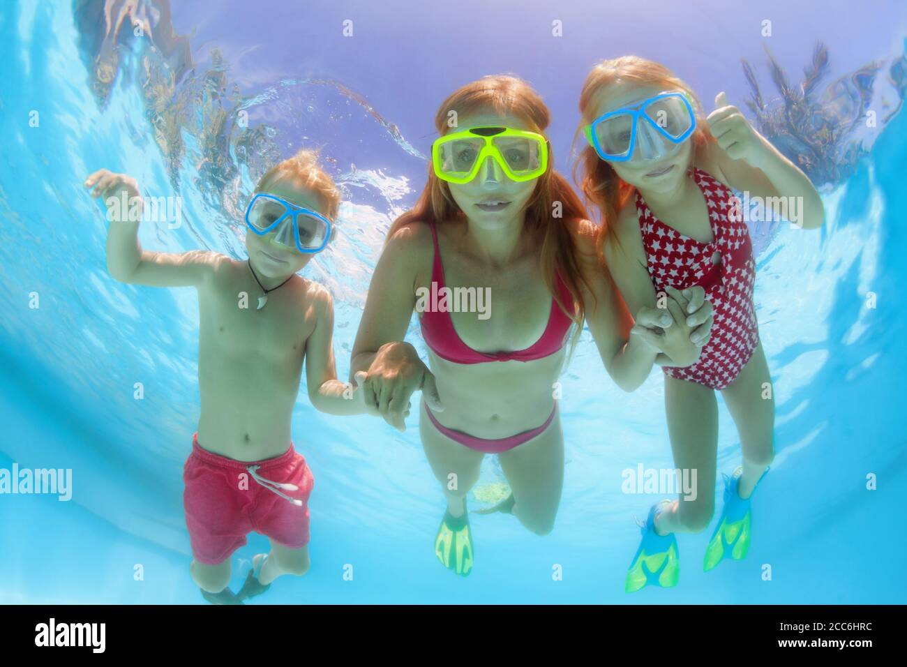 Les gens heureux plongent sous l'eau avec plaisir. Drôle de photo de mère, les enfants dans les masques de plongée avec masque et tuba dans la piscine du parc aquatique. Mode de vie familial, activité aquatique Banque D'Images