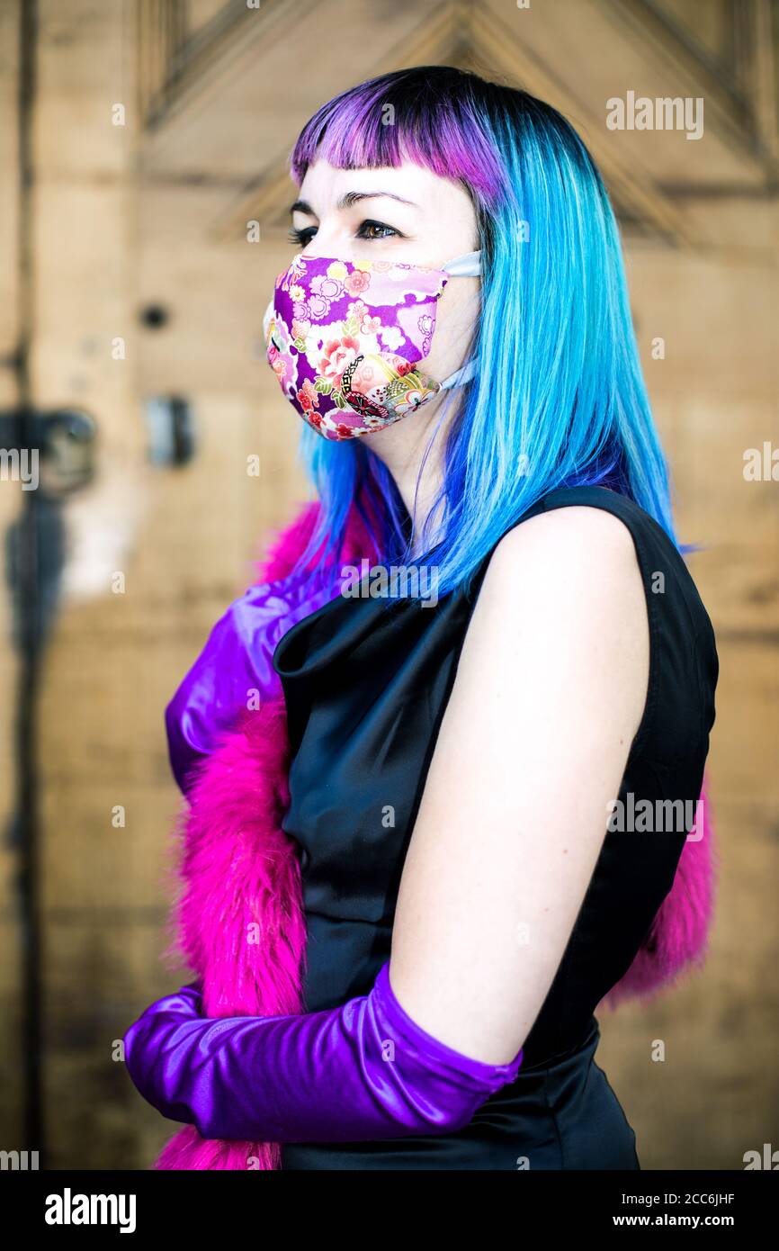 Femme avec la mode colorée debout devant de grands bois Portes portant un masque dans un climat Covid-19 Banque D'Images