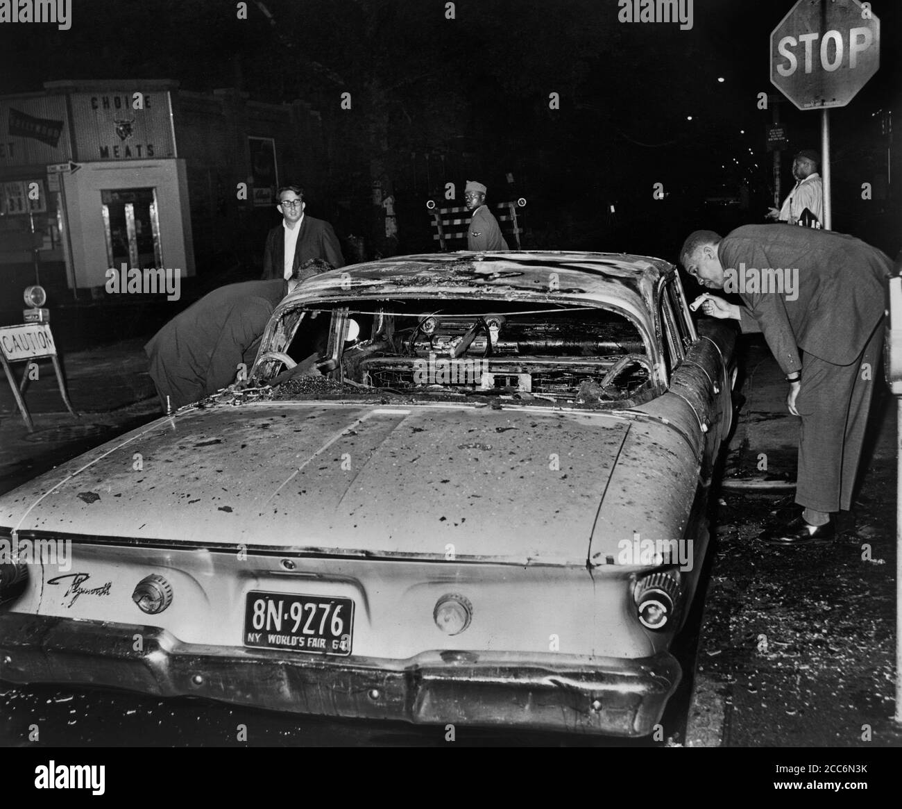 Un détective examine une voiture de police brûlée après la nuit d'émeutes à cause d'une fusillade fatale de Teen James Powell par le policier Lt. Thomas Gilligan, Herkimer Street et Nostrand Avenue, Brooklyn, New York, États-Unis, Stanley Wolfson, World Telegram & Sun, juillet 1964 Banque D'Images