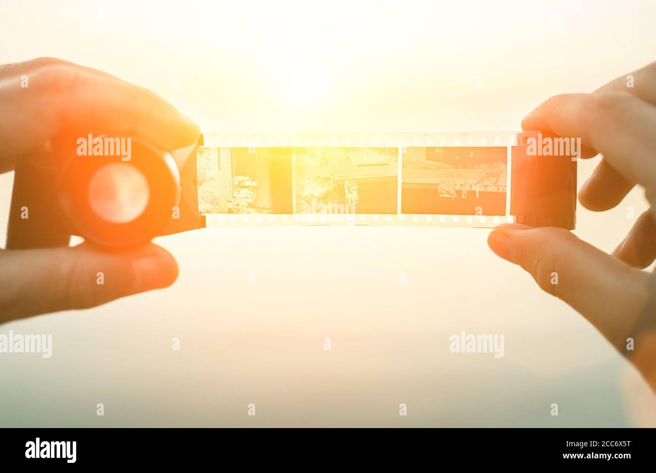Image des mains de sexe masculin utilisant le négatif de film 35 mm ancien Viewer pour voir une image sur l'arrière-plan du coucher de soleil Banque D'Images