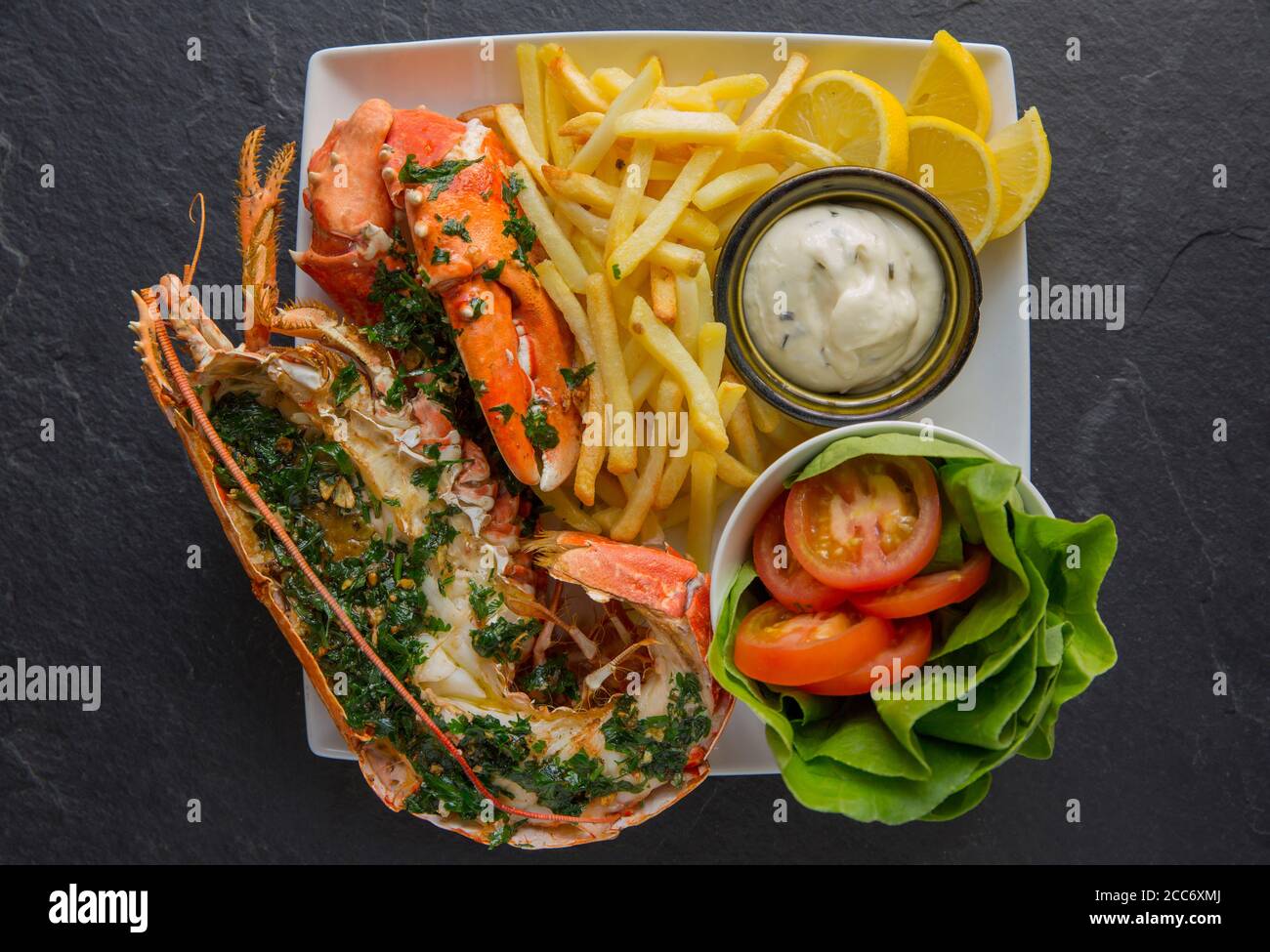 Un demi-homard, Homarus gammarus, qui a été grillé et assaisonné avec une sauce au beurre, à l'ail et au persil et servi avec des frites et de la salade. Le lobs Banque D'Images