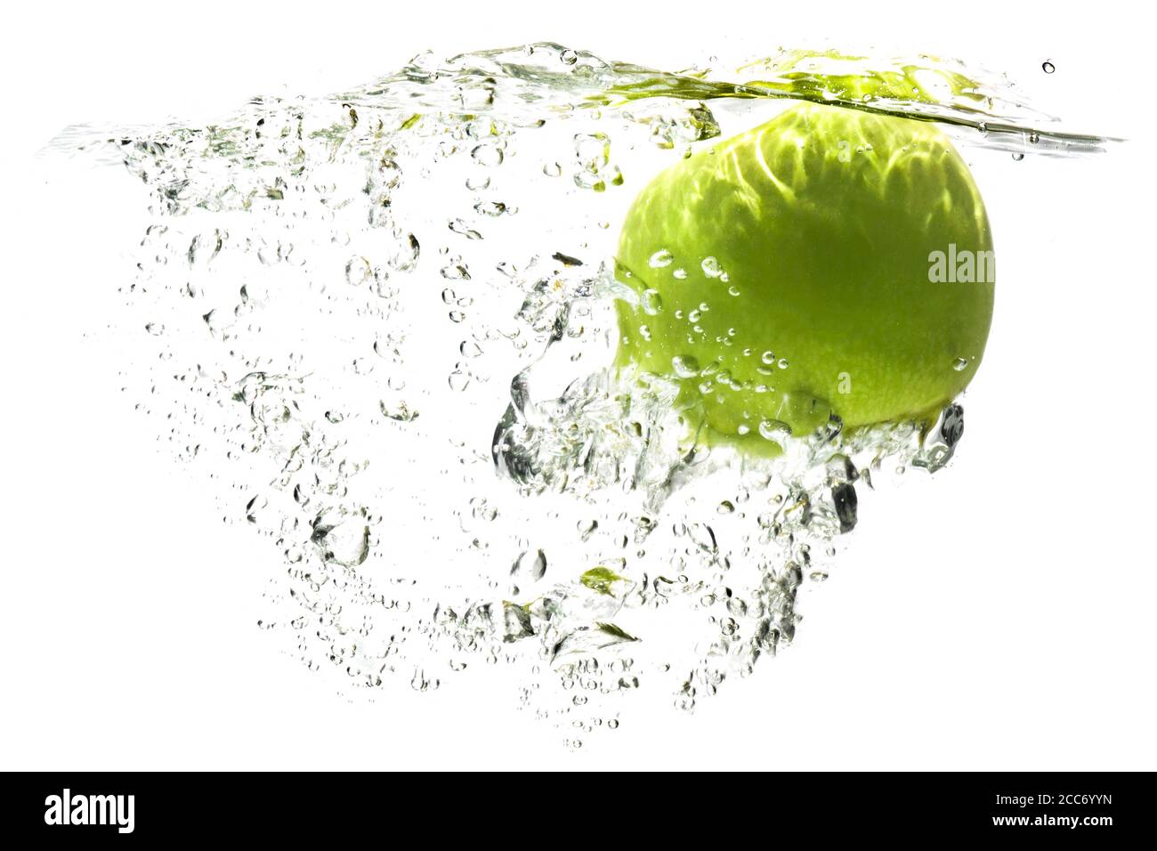 une pomme verte tombant dans l'eau sur un fond blanc avec des éclaboussures, des gouttes et des bulles. Banque D'Images