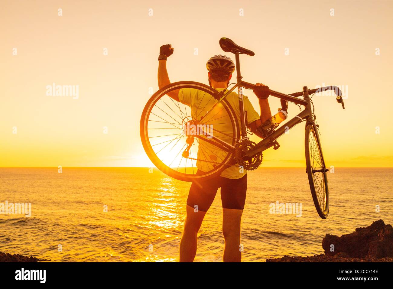 Le succès, la réussite et le concept gagnant avec cycliste homme sur route. Joyeux athlète professionnel de vélo levant les bras de levage vélo par mer pendant Banque D'Images