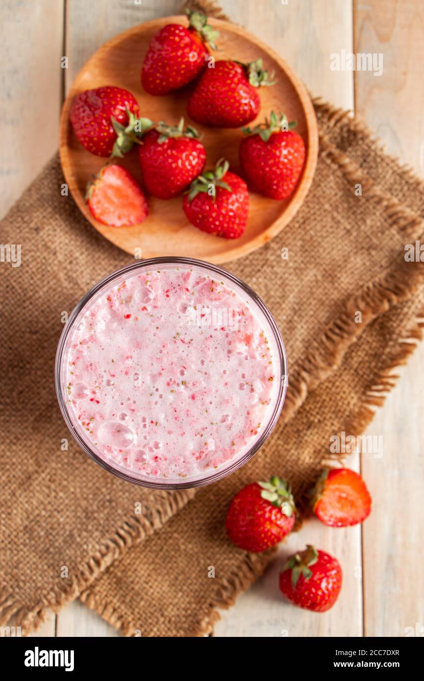 Milk-shake frais avec fraises. Boisson d'été avec baies dans un verre sur fond de bois. Photo verticale Banque D'Images