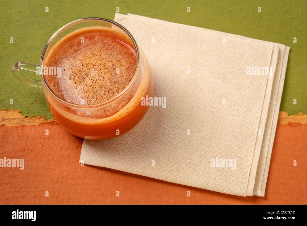 une tasse de verre de jus de carotte frais fait maison sur une serviette contre papier coloré résumé, concept de saine alimentation Banque D'Images