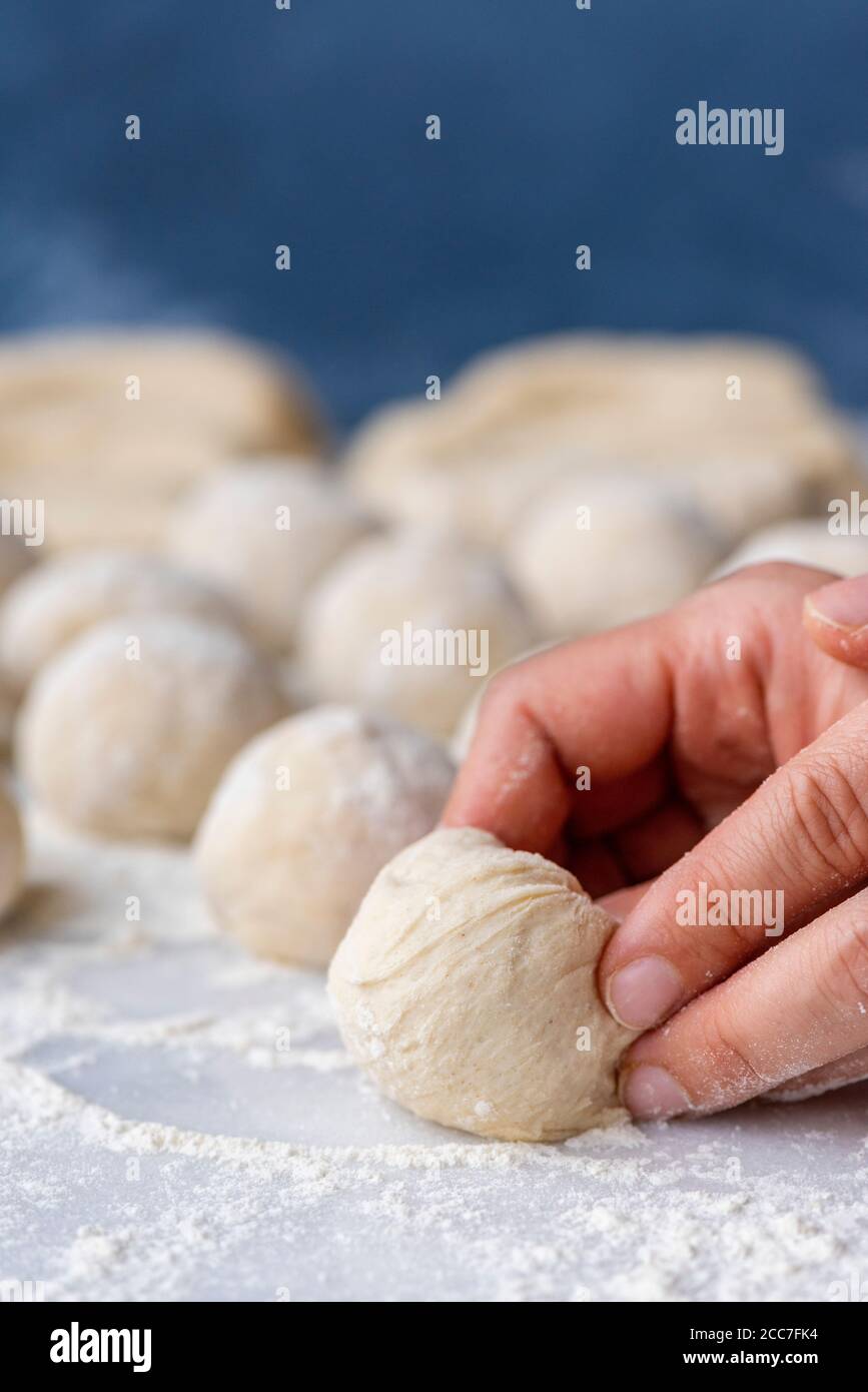 Femme façonnant des boules de pâte sur une surface en marbre saupoudrées de farine. Banque D'Images