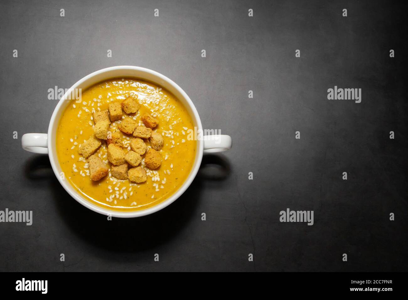 Soupe de crème de citrouille avec craquelins sur fond sombre. Soupe de crème de citrouille avec craquelins dans un bouillon blanc sur fond sombre, assiette pour le texte Banque D'Images