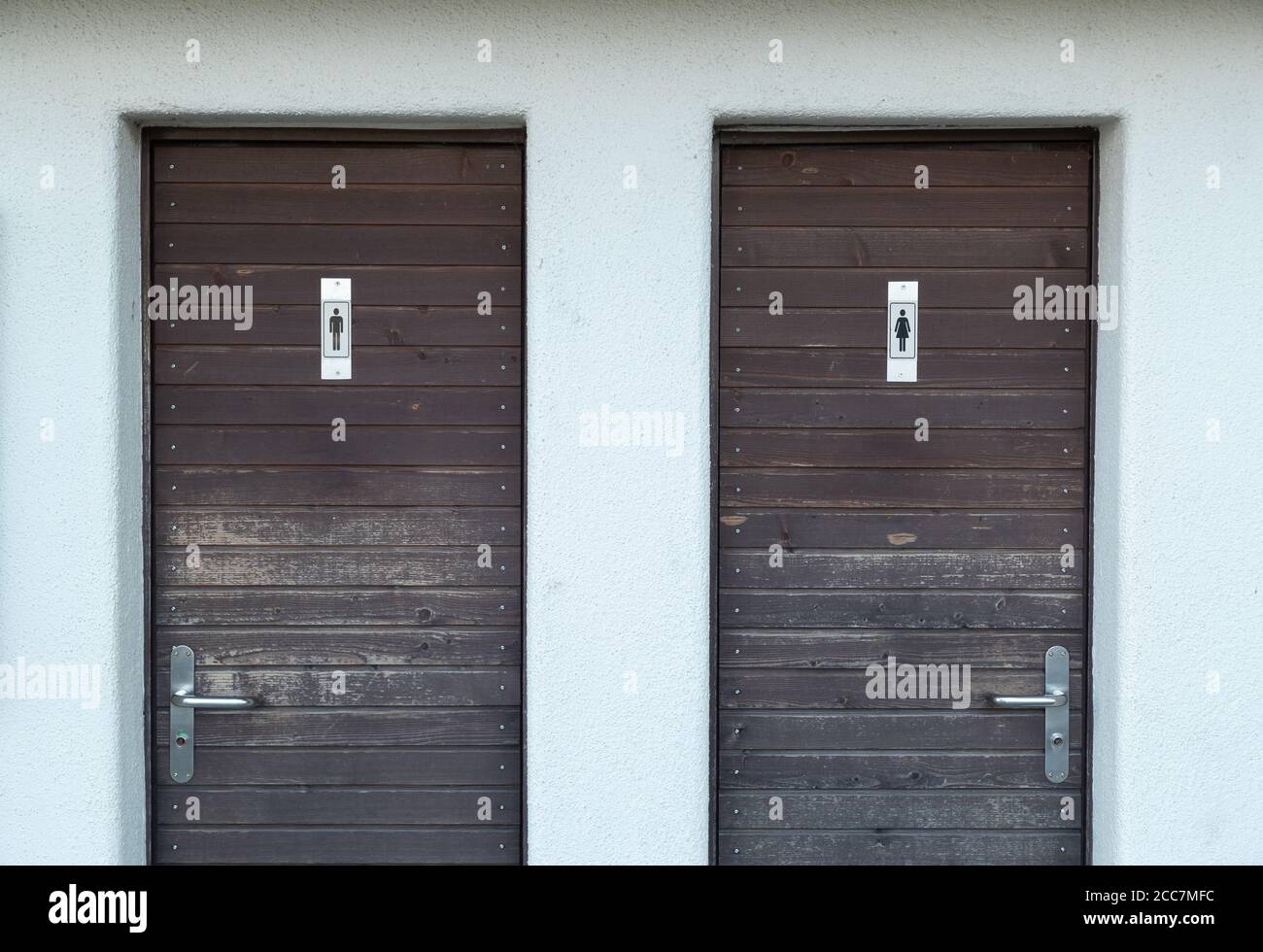 deux portes de toilettes en bois marron avec le symbole homme et femme sur la porte, un mur en plâtre blanc entoure les portes, un signal vert sur la poignée de porte Banque D'Images