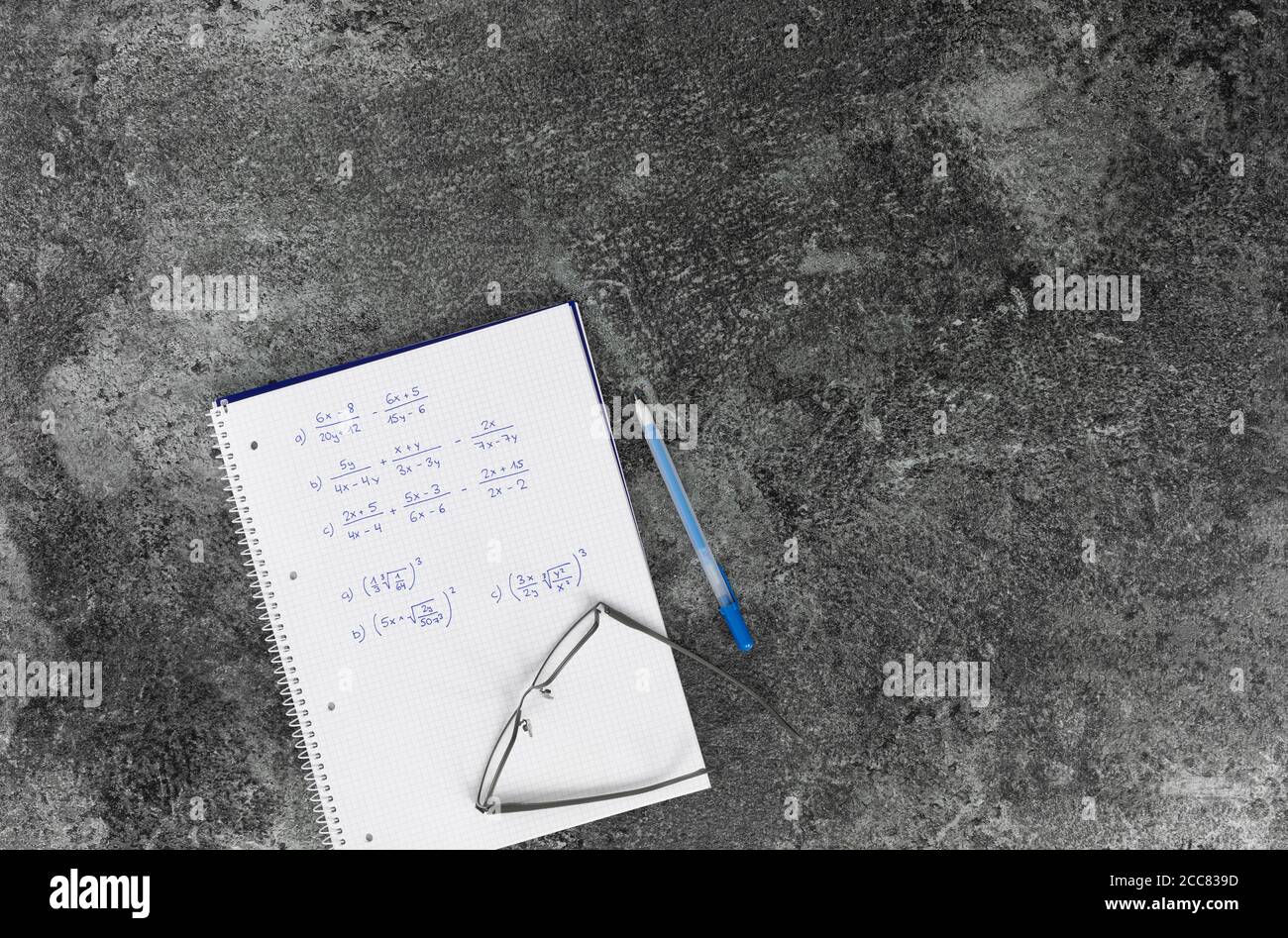 Livre de mathématiques avec problèmes arithmétiques, lunettes, stylo bleu sur une table en marbre gris Banque D'Images
