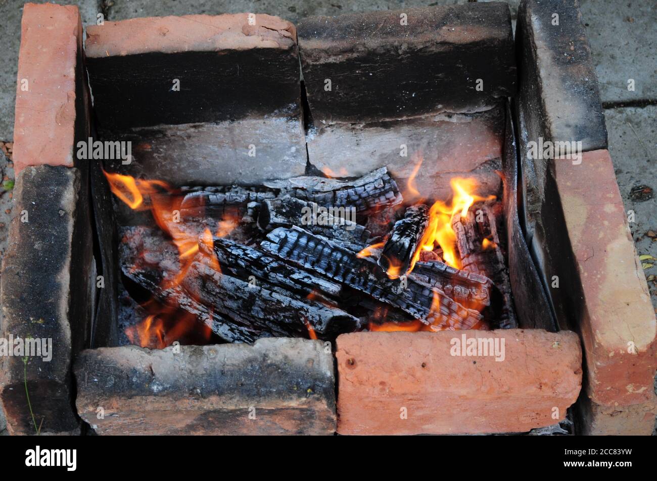 Bois de chauffage fissuré couvant avec des flammes de couleur orange parmi les cendres. Briques charrées de couleur rouge terre cuite et noir fumé dans un ancien brazier de charbon de bois. Bois de charRed Banque D'Images