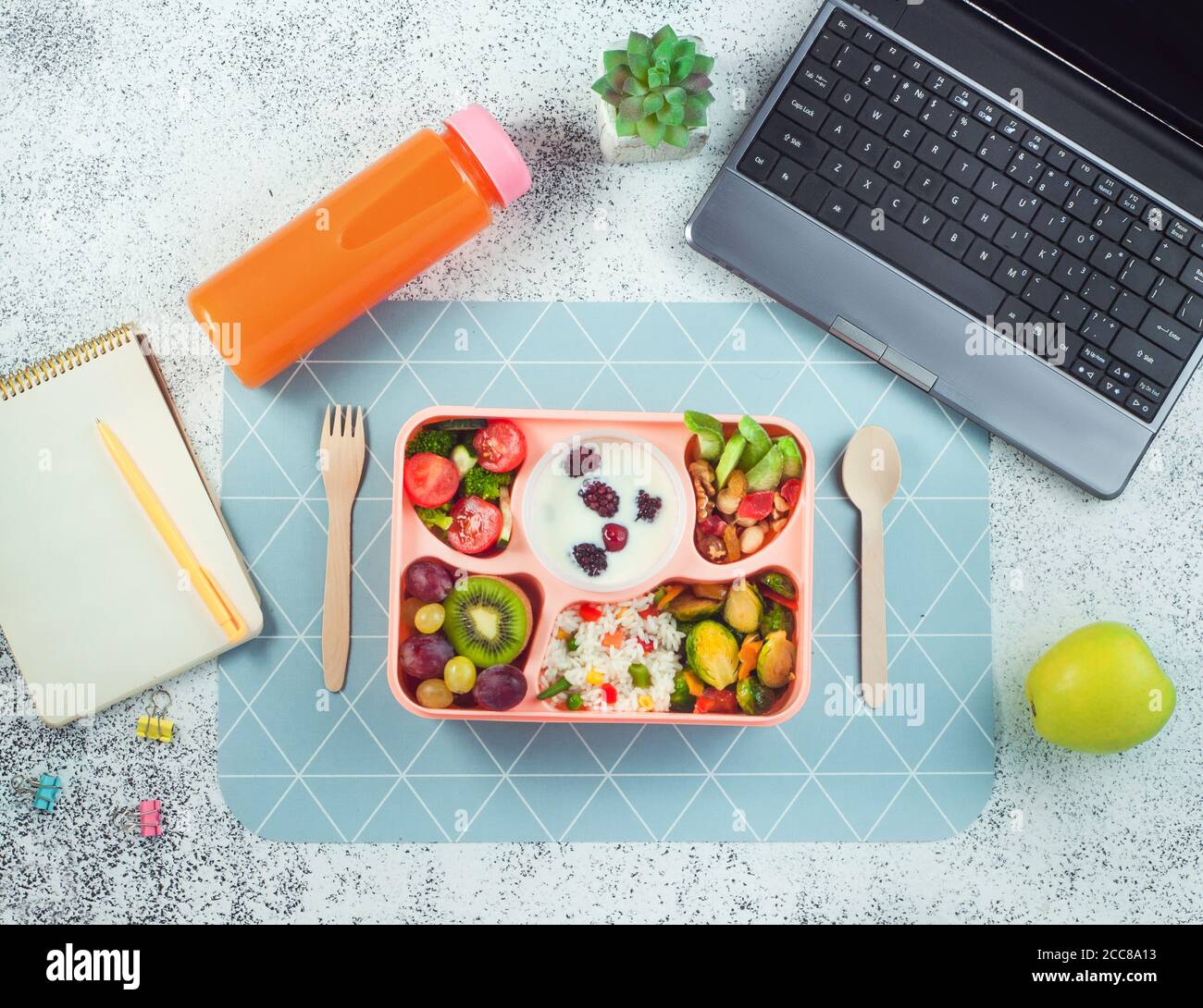 Panier repas avec riz, légumes et fruits, baies de yougurt sur table de bureau près de l'ordinateur portable Banque D'Images