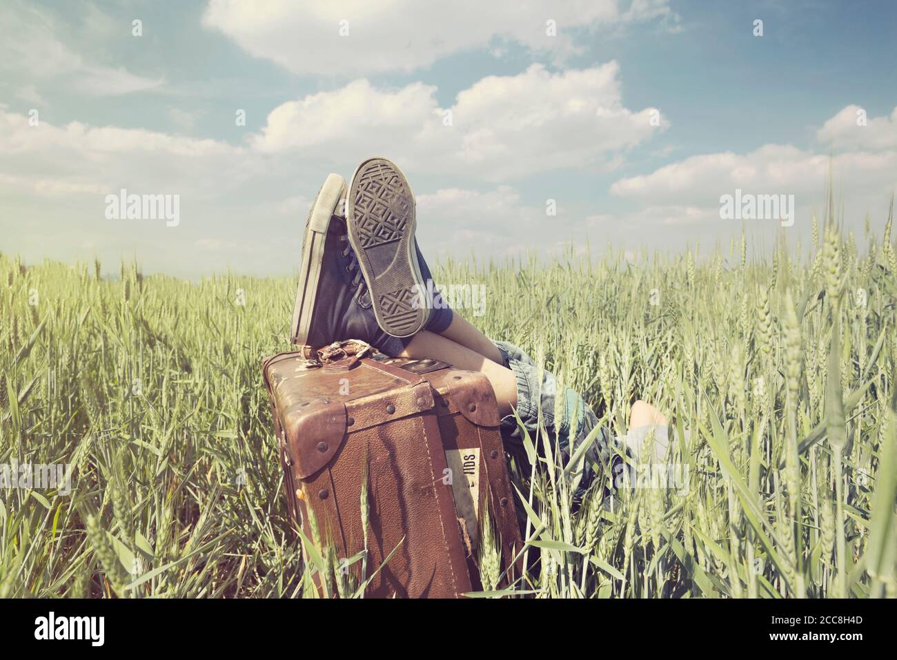 Jeune garçon se reposant dans un pré avec ses pieds au-dessus sa valise Banque D'Images