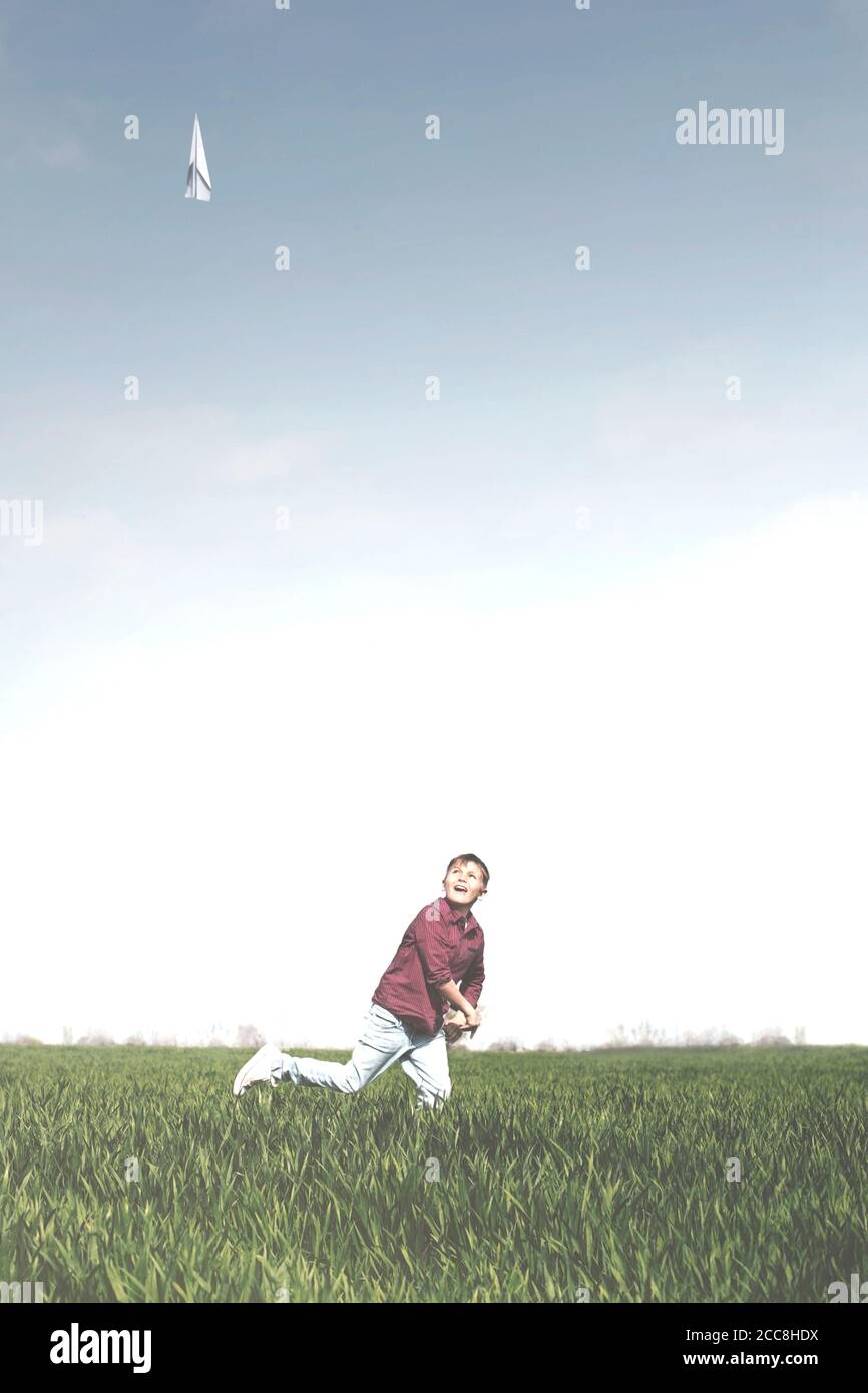 un jeune garçon court dans la prairie en lançant son nouveau papier avion dans les airs Banque D'Images