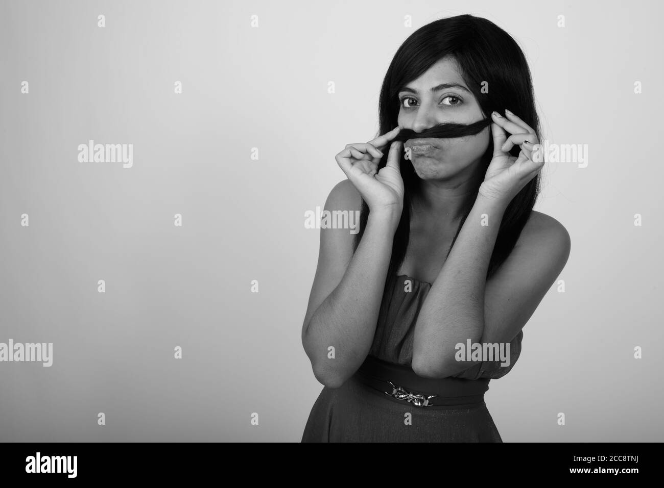 Photo en studio d'une jeune femme persane utilisant les cheveux comme moustache tout en portant la robe sur fond gris Banque D'Images Photo en studio d'une jeune femme persane utilisant les cheveux comme moustache tout en portant la robe sur fond gris Banque D'Images