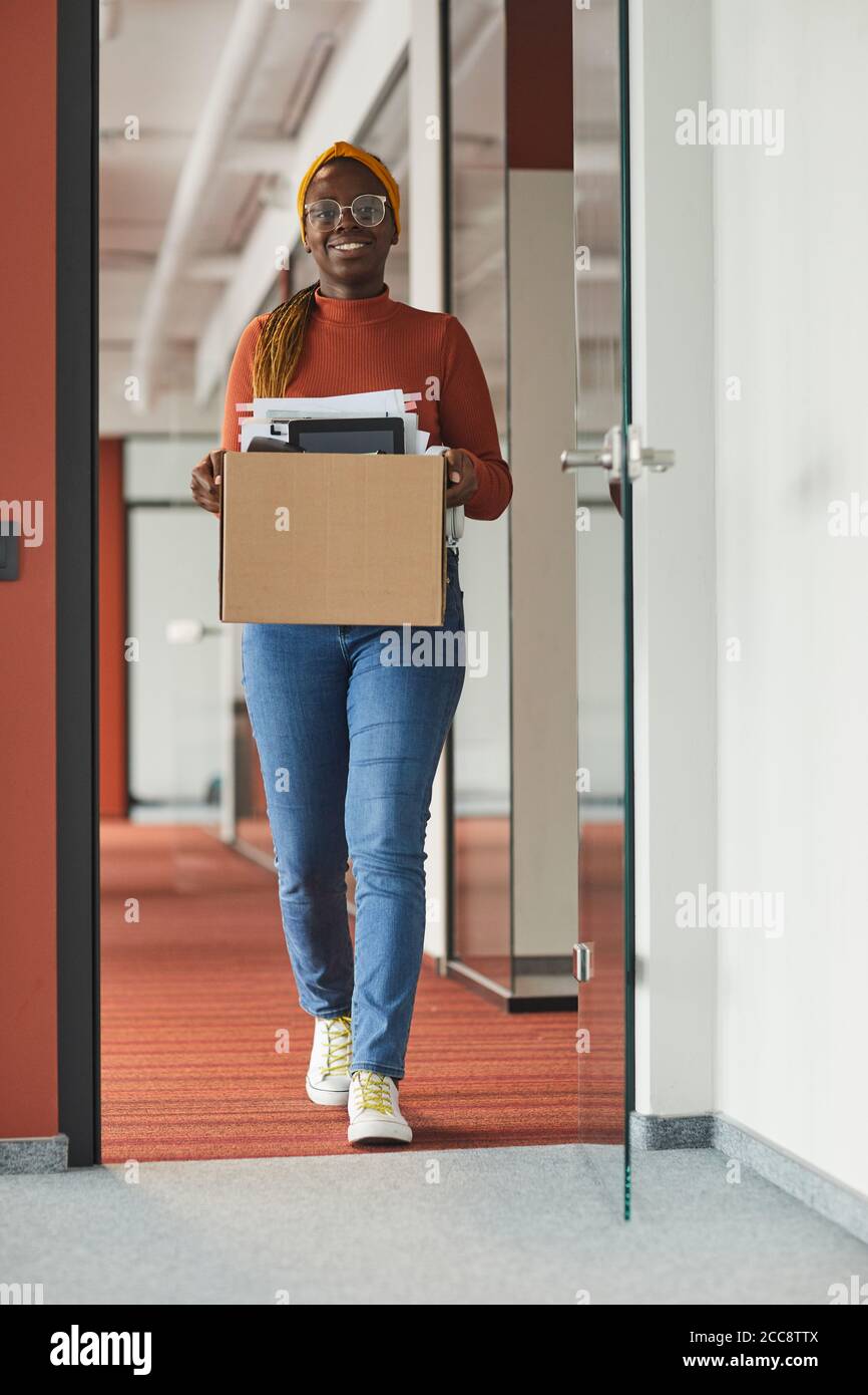 Femme d'affaires africaine heureuse portant sa boîte avec les produits de bureau qu'elle quitte le bureau Banque D'Images