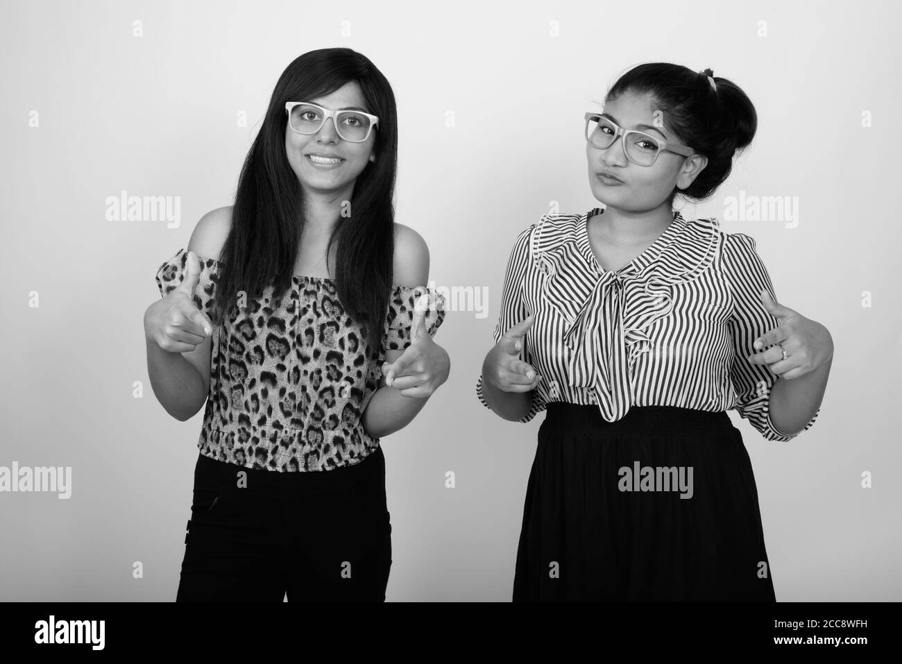 Deux jeunes femmes persanes heureuses pointent les deux doigts vers la caméra et porter des lunettes ensemble Banque D'Images