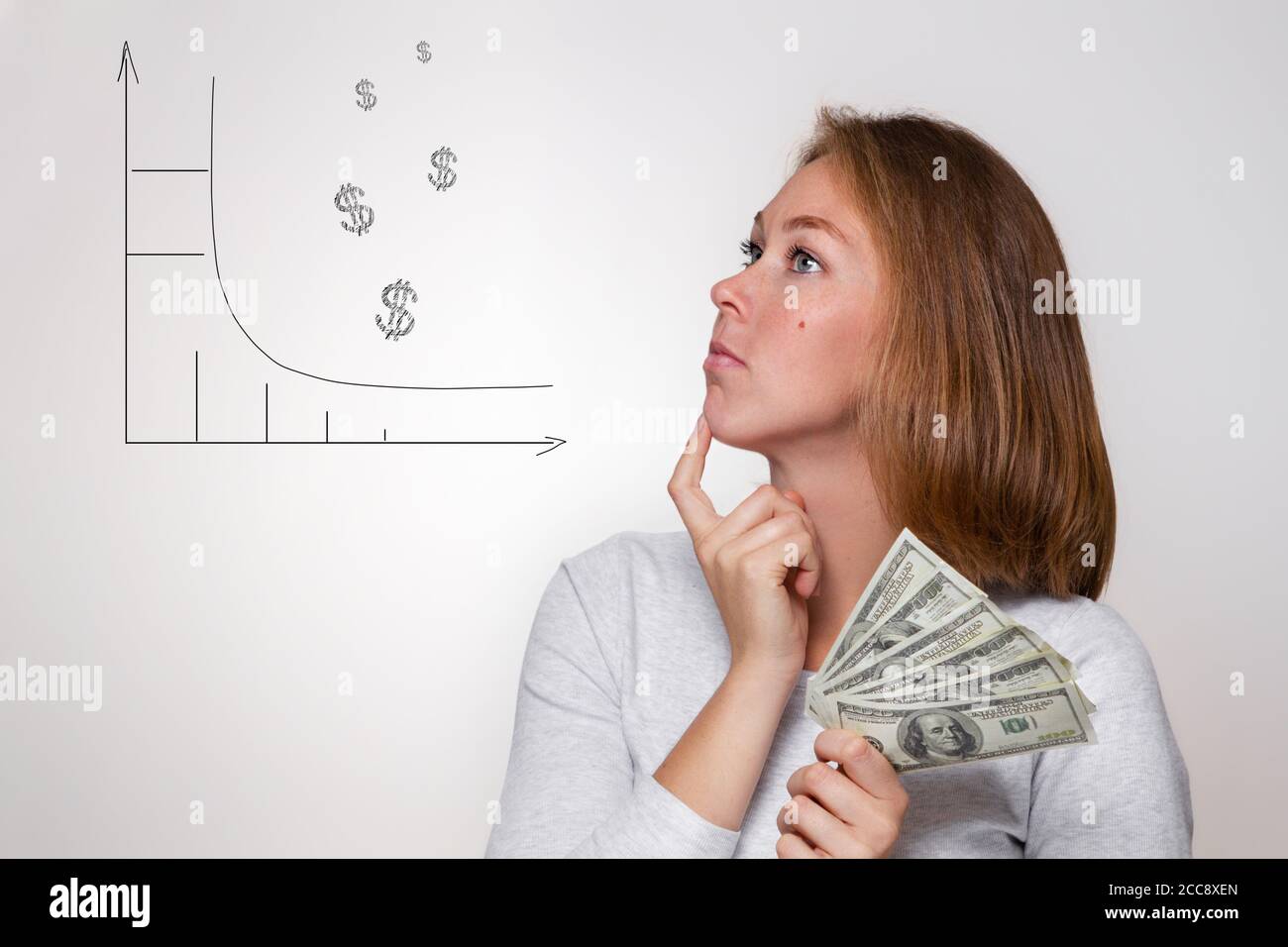Finance et banque. Une jeune blonde tient une wad de dollars dans ses mains et regarde attentivement le diagramme dessiné. Arrière-plan blanc. Banque D'Images