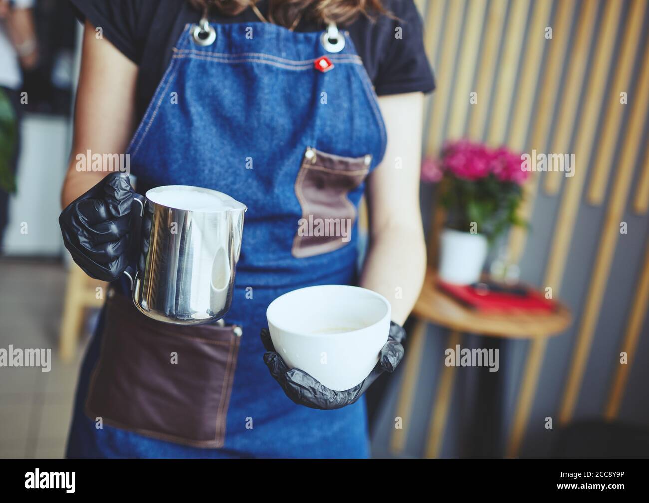La femme tient un pot à lait et une tasse de café, prépare du cappuccino et verse du lait fouetté dans un espresso Banque D'Images