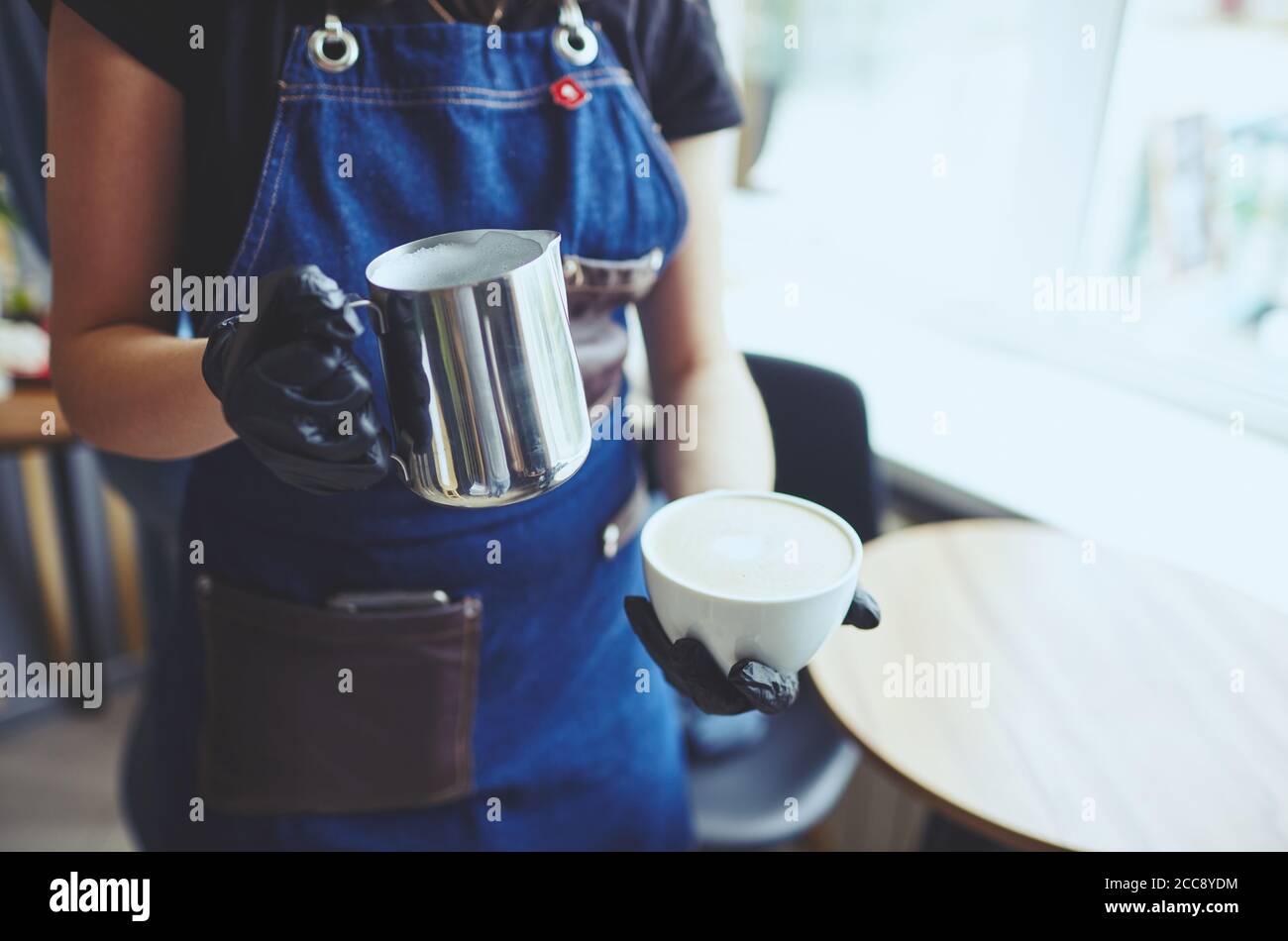 La femme tient un pot à lait et une tasse de café, prépare du cappuccino et verse du lait fouetté dans un espresso Banque D'Images