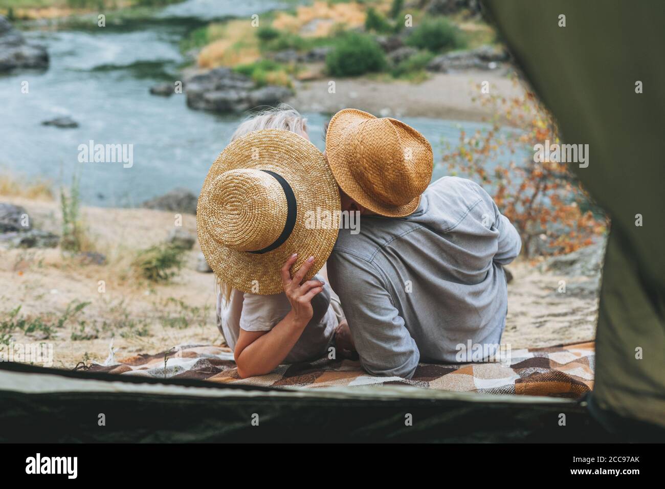 Joyeux jeune couple voyageurs dans des tenues décontractées embrassant près de la tente dans les montagnes. Tourisme local, concept de voyage de week-end Banque D'Images