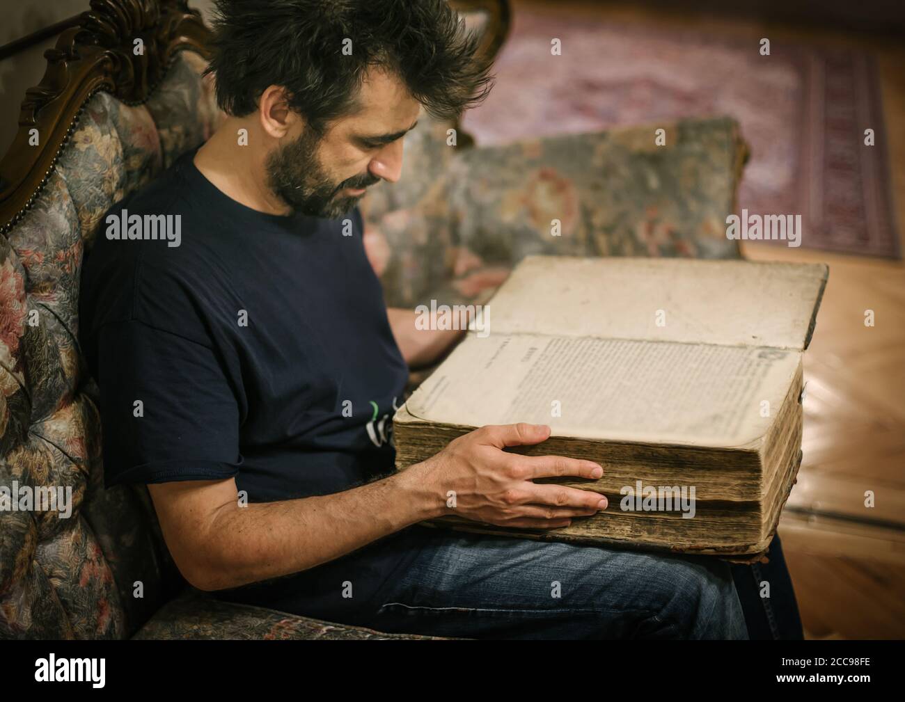 Curieux homme lisant un vieux livre dans sa bibliothèque à la maison. Style rétro Banque D'Images