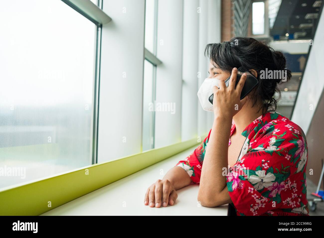 femme à l'aéroport portant un masque de protection chirurgical, parlant au téléphone souriant et positif, voyageant pendant la pandémie de covid-19 Banque D'Images