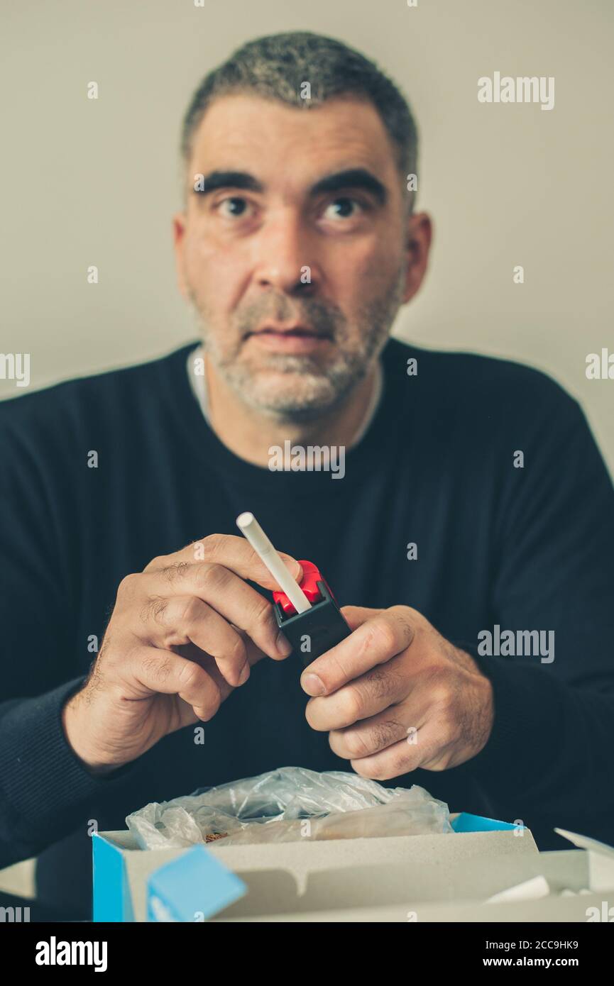 Smoker man roule des cigarettes de tabac domestique à l'aide d'une machine à rouler. Gros plan Banque D'Images