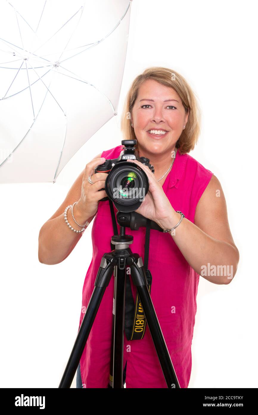Portrait vertical d'un photographe utilisant un appareil photo reflex numérique sur un trépied et une lumière pour prendre des photos en studio. Banque D'Images
