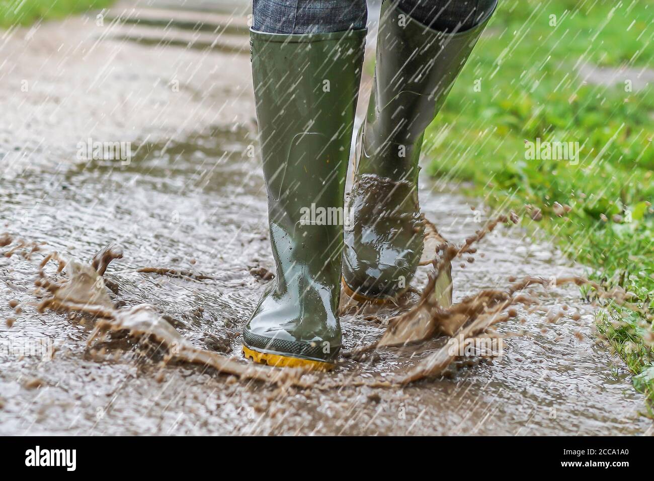 Fermer, vue de face des bottes wellington vertes isolées portées par une femme éclaboussant à travers les flaques d'eau dans un chemin de campagne, dans la douche de pluie d'été lourde, Royaume-Uni. Banque D'Images