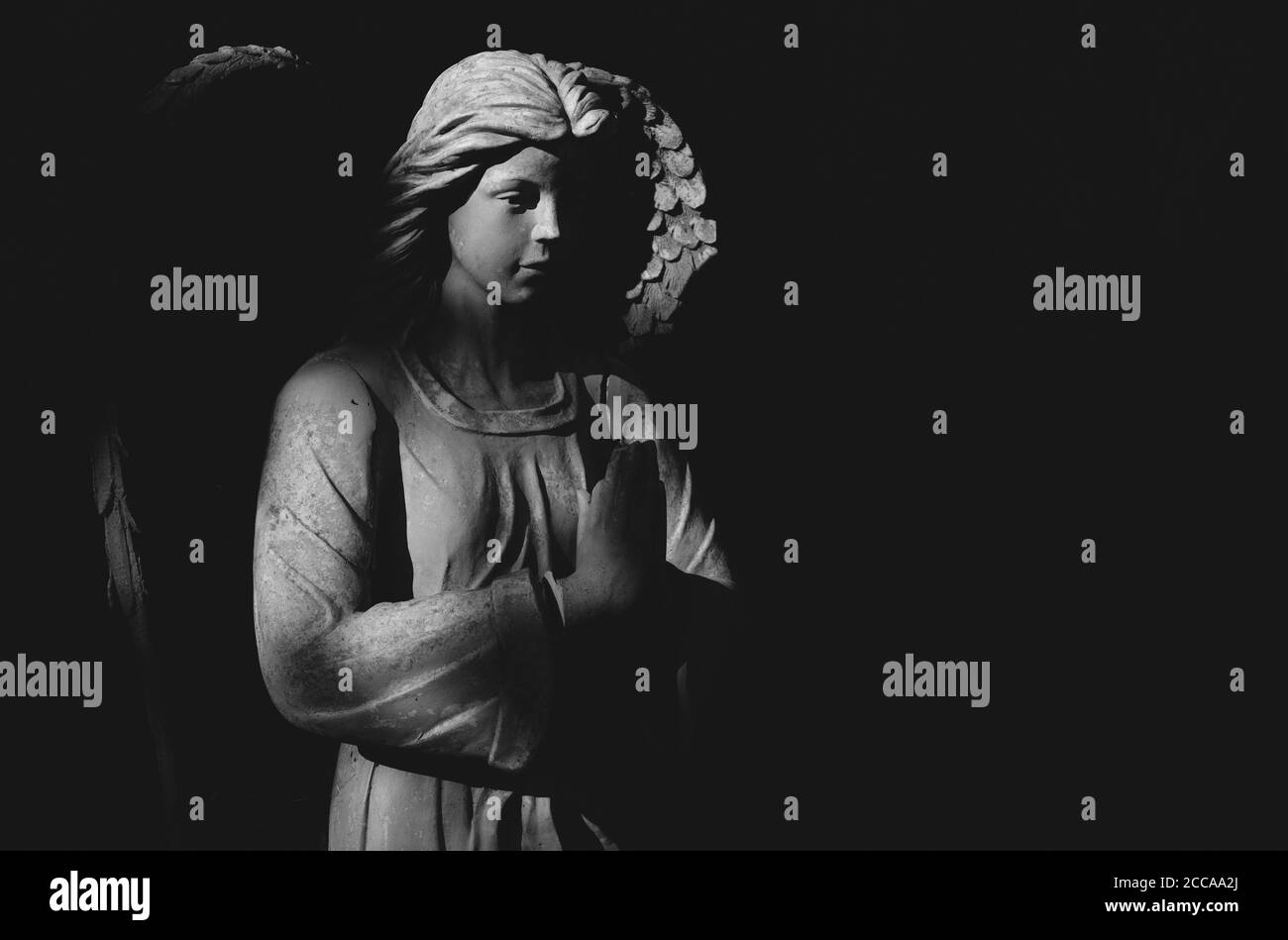 Statue d'ange priant dans la lumière et l'ombre. Image en noir et blanc. Banque D'Images