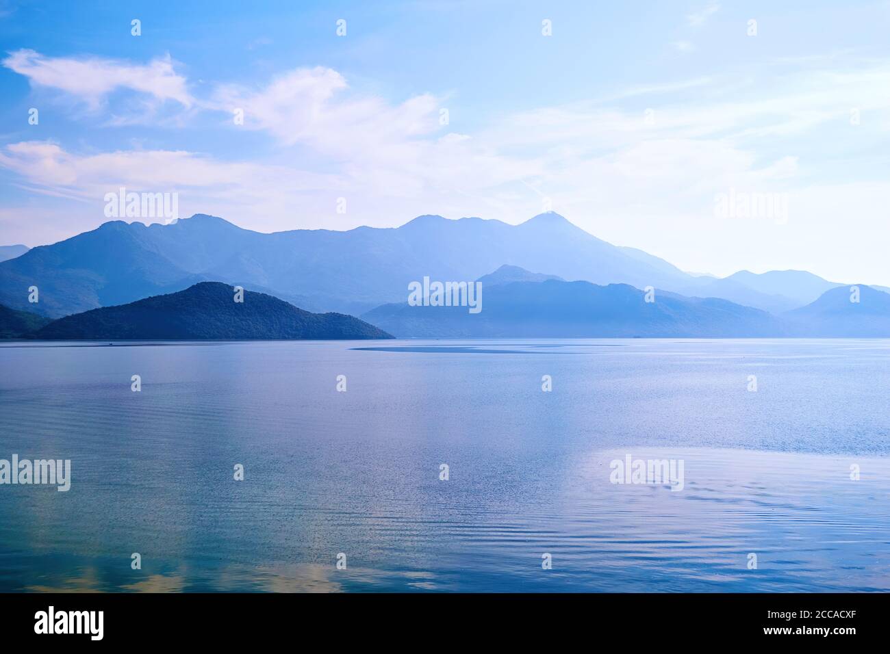 Crépuscule sur l'eau calme du lac et île avec des montagnes. Célèbre lac de Skadar au Monténégro. Texture d'arrière-plan de la nature Banque D'Images
