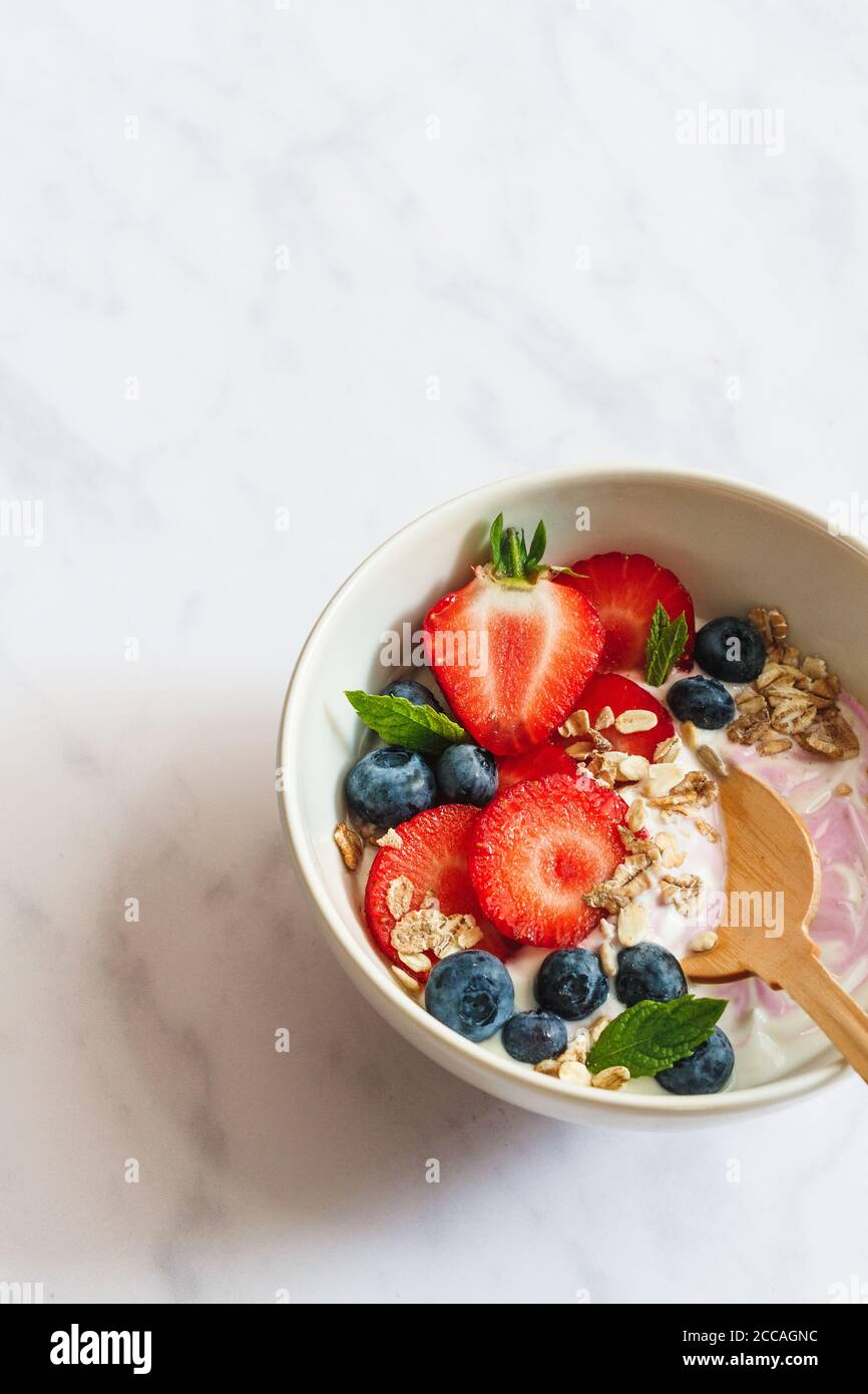 Petit déjeuner en été. Bol de yaourt avec fraises, bleuets et muesli sur fond de marbre blanc. Banque D'Images