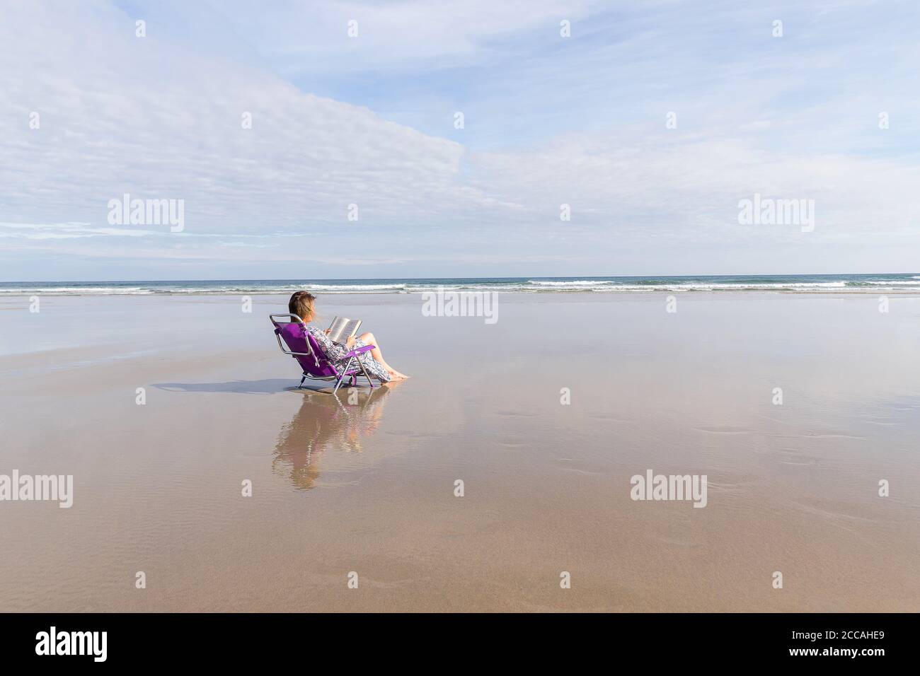 Femme pieds nus lisant un livre assis sur une chaise sur la plage. Copier l'espace. Concept de distance sociale. Banque D'Images