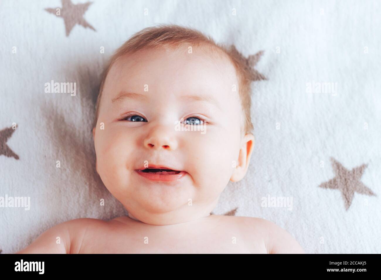 Photo D Un Bebe Souriant D Un Nouveau Ne Aux Yeux Bleus Et Aux Cheveux Blonds Allonge Sur Une Couverture Lumineuse Aux Etoiles Brunes Photo Stock Alamy