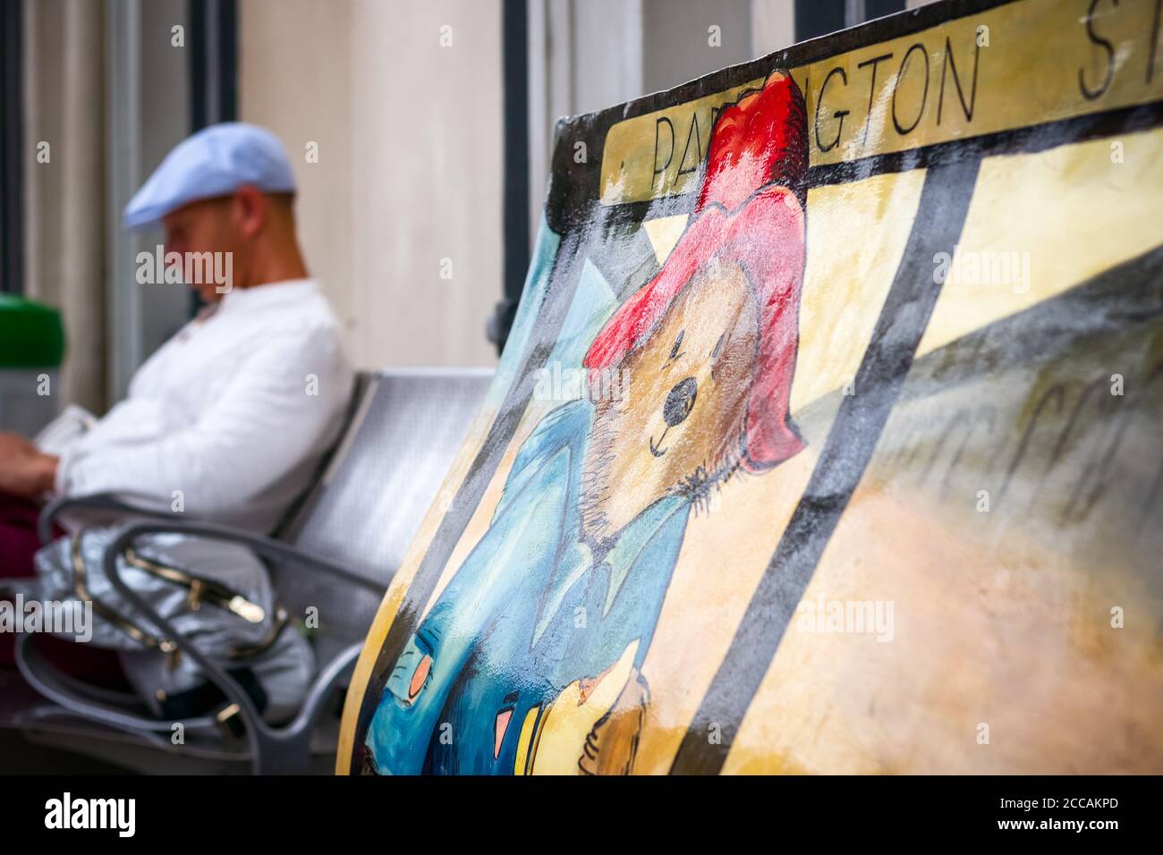 Londres, Royaume-Uni - 17 avril 2019 - Paddington Bear Book Bench sculptures à la gare de Paddington avec un voyageur en arrière-plan Banque D'Images