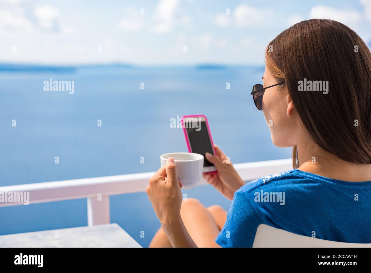 Téléphone matin petit déjeuner femme buvant une tasse de café sur l'Europe été vacances relaxantes fille au café lisant le téléphone portable à la terrasse extérieure Vue sur l'océan Banque D'Images