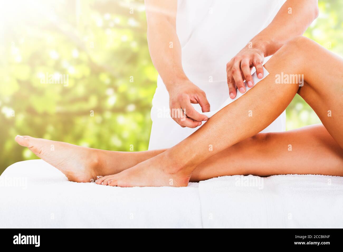 Section médiane de la Beauticienne cirant la jambe de la femme avec bande de cire à Spa de beauté Banque D'Images
